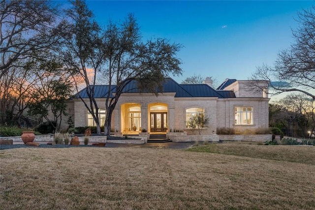 view of front of home with a standing seam roof, french doors, a front yard, metal roof, and a chimney