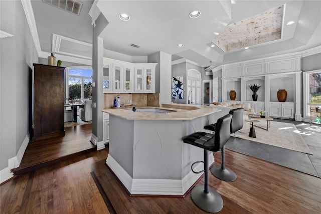 kitchen with visible vents, a breakfast bar, dark wood-style flooring, white cabinets, and glass insert cabinets