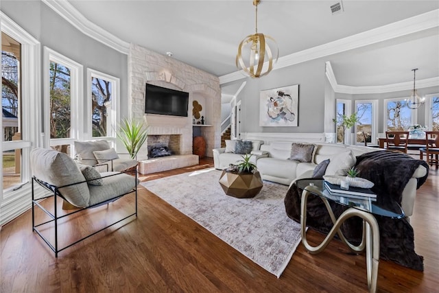 living room featuring visible vents, ornamental molding, wood finished floors, a large fireplace, and an inviting chandelier