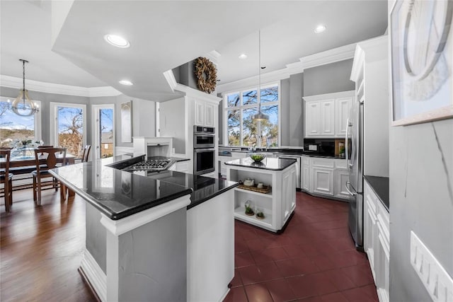 kitchen featuring a kitchen island, stainless steel appliances, an inviting chandelier, white cabinets, and crown molding