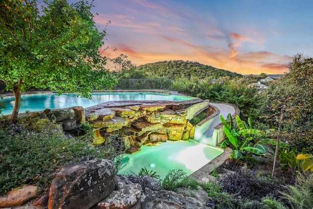 pool at dusk featuring a pool with connected hot tub