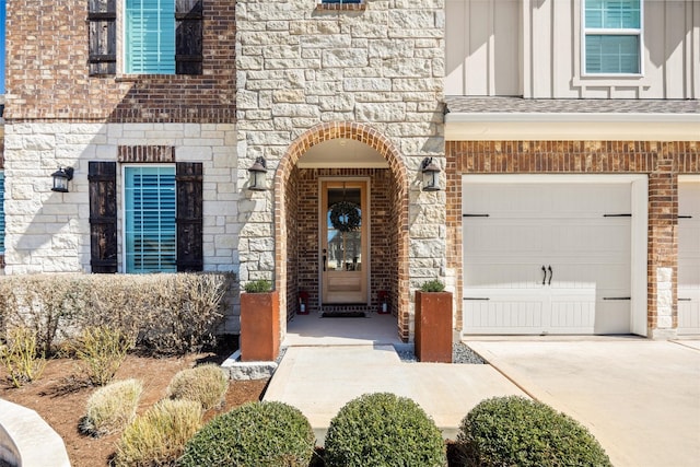 entrance to property featuring driveway, brick siding, stone siding, a garage, and board and batten siding