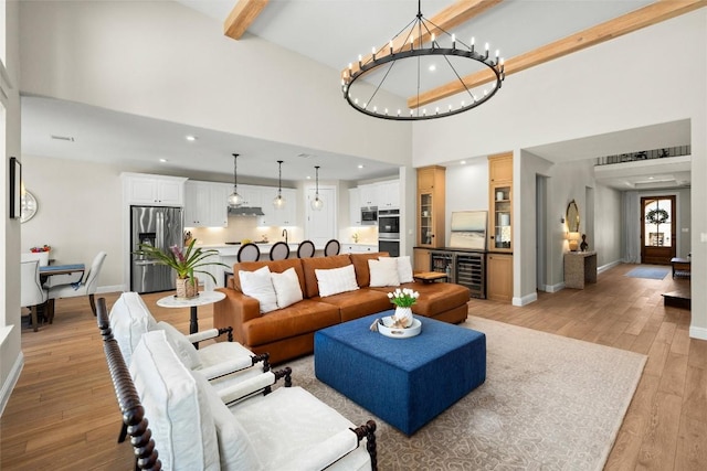 living room with baseboards, an inviting chandelier, a high ceiling, light wood-style flooring, and beam ceiling