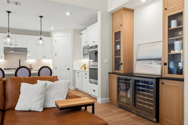 kitchen with visible vents, light wood-type flooring, under cabinet range hood, tasteful backsplash, and hanging light fixtures