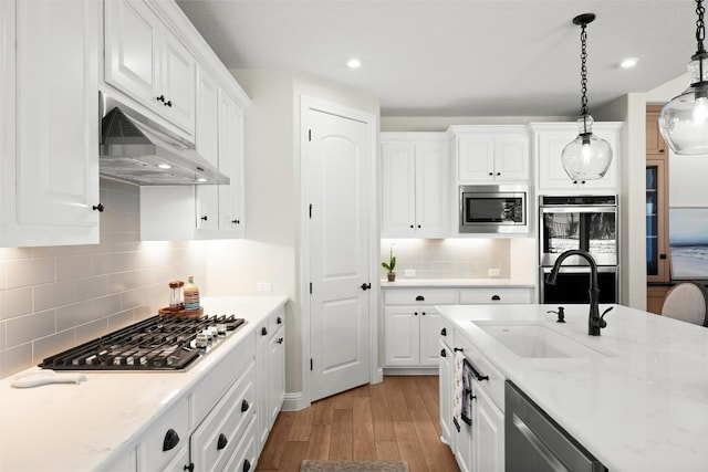 kitchen with under cabinet range hood, appliances with stainless steel finishes, wood finished floors, white cabinets, and a sink