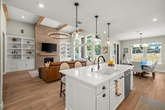 kitchen featuring light wood finished floors, a stone fireplace, an inviting chandelier, and a sink