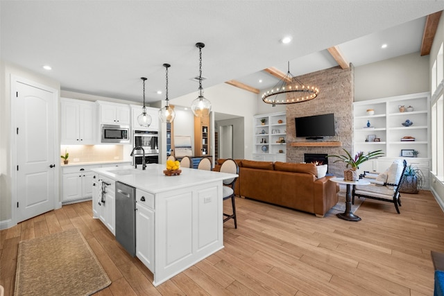 kitchen with light wood finished floors, a breakfast bar area, a fireplace, stainless steel appliances, and a sink