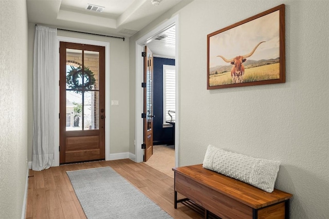 entrance foyer featuring a tray ceiling, wood finished floors, visible vents, and a textured wall