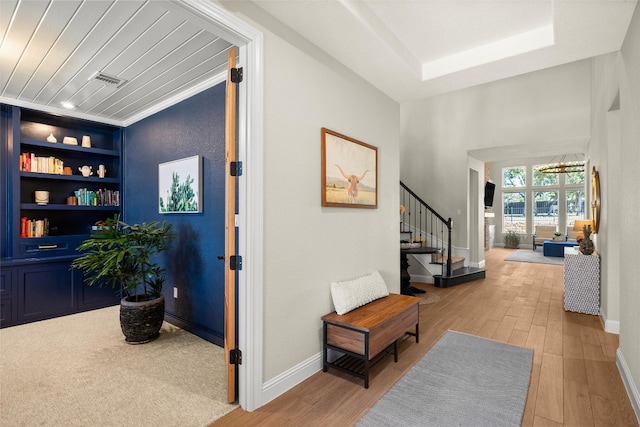 corridor featuring built in features, light wood-type flooring, stairs, and baseboards