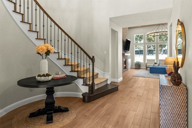 entryway with a glass covered fireplace, a notable chandelier, wood finished floors, and a towering ceiling