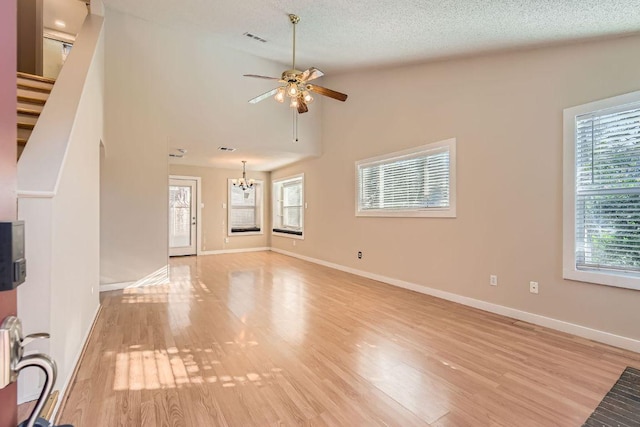 unfurnished living room featuring visible vents, baseboards, light wood-type flooring, ceiling fan with notable chandelier, and a textured ceiling