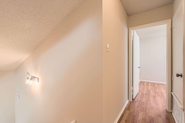 corridor featuring light wood-type flooring, baseboards, and a textured ceiling