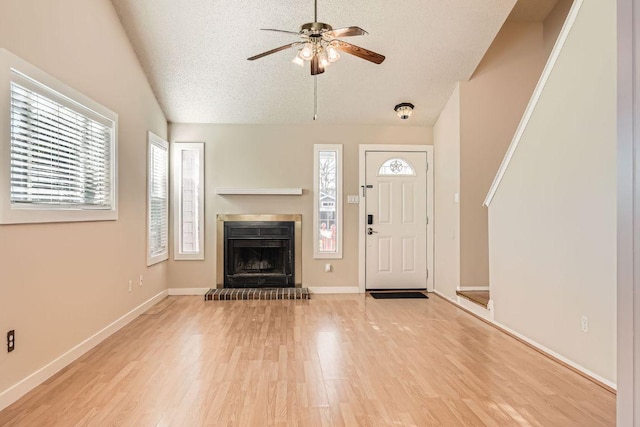 entryway featuring baseboards, light wood finished floors, ceiling fan, vaulted ceiling, and a textured ceiling