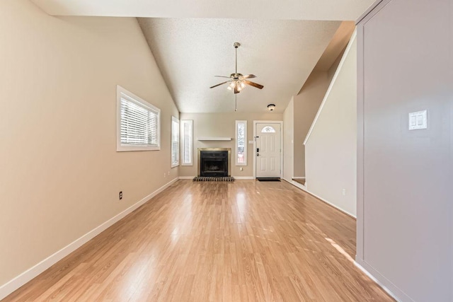 unfurnished living room with light wood finished floors, a brick fireplace, baseboards, and ceiling fan