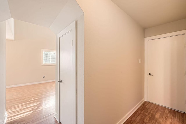 hall featuring baseboards, lofted ceiling, and wood finished floors