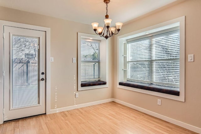 unfurnished dining area featuring light wood finished floors, an inviting chandelier, and baseboards