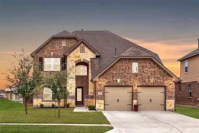 french country style house with brick siding, a front lawn, roof with shingles, a garage, and stone siding