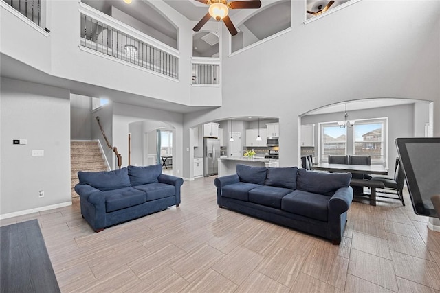 living area featuring arched walkways, stairway, ceiling fan with notable chandelier, and baseboards