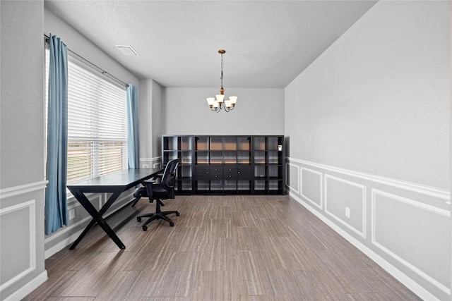 office space with visible vents, wood finished floors, a chandelier, and a decorative wall