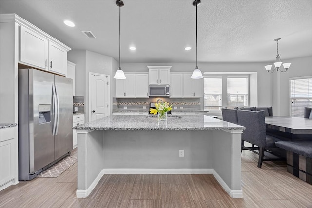 kitchen with visible vents, a breakfast bar, stainless steel appliances, white cabinets, and decorative backsplash