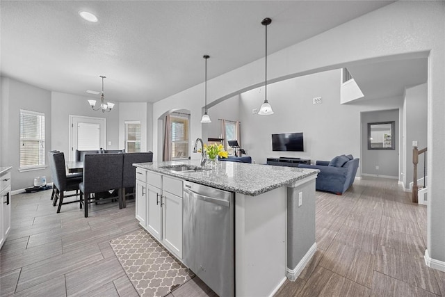 kitchen featuring a center island with sink, stainless steel dishwasher, white cabinetry, light stone countertops, and wood tiled floor