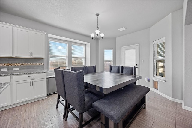 dining area featuring visible vents, baseboards, wood finish floors, a chandelier, and a textured ceiling