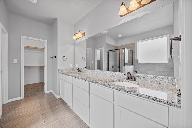 bathroom featuring a shower stall, a spacious closet, double vanity, and a sink