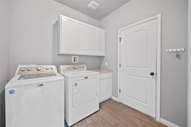 washroom featuring light wood-style flooring, cabinet space, baseboards, and washer and clothes dryer