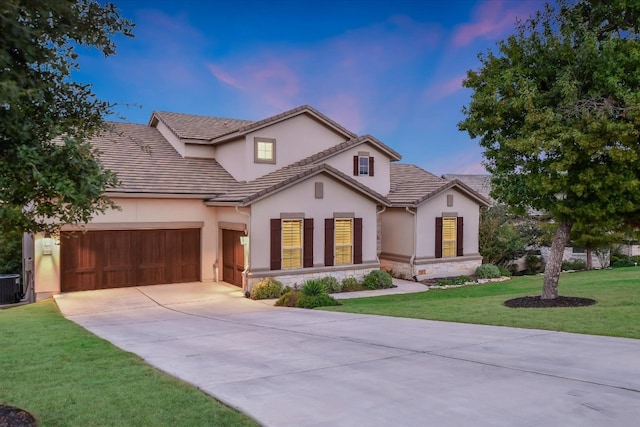 mediterranean / spanish-style home featuring stucco siding, driveway, a front lawn, stone siding, and an attached garage