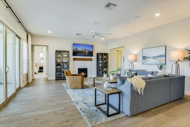 living area with a stone fireplace, light wood-style flooring, recessed lighting, and a ceiling fan