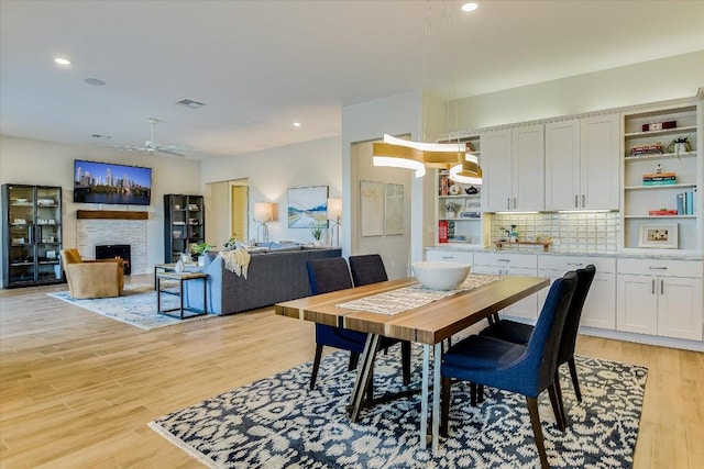 dining area with ceiling fan, visible vents, a lit fireplace, and light wood-style flooring