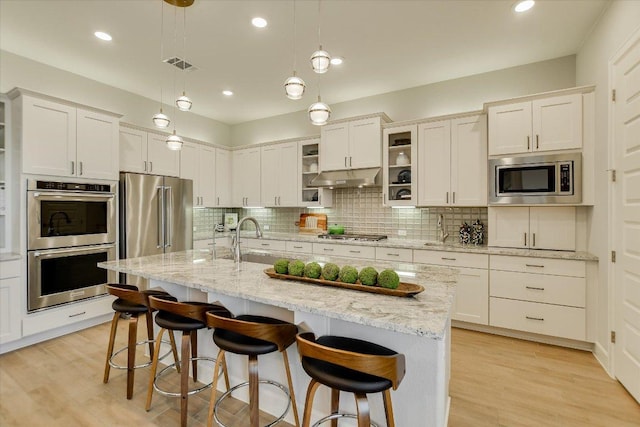 kitchen featuring visible vents, under cabinet range hood, appliances with stainless steel finishes, a kitchen breakfast bar, and backsplash