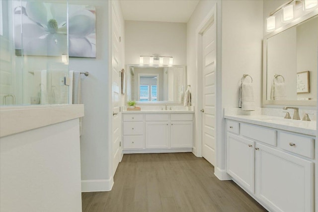 bathroom featuring two vanities, wood finished floors, a stall shower, and a sink