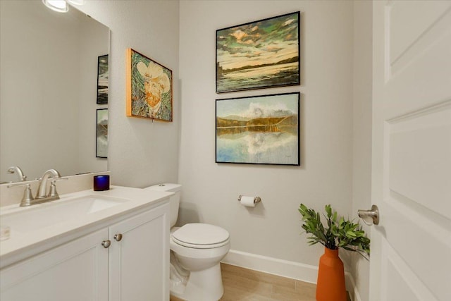 half bathroom featuring baseboards, toilet, wood finished floors, and vanity