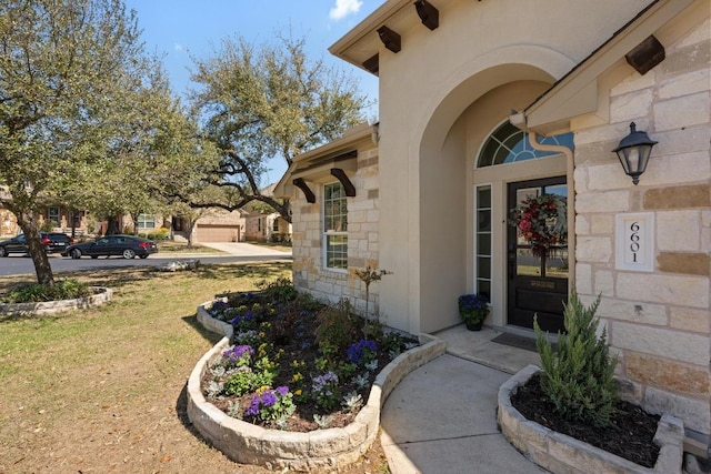 doorway to property with stucco siding, stone siding, and a lawn