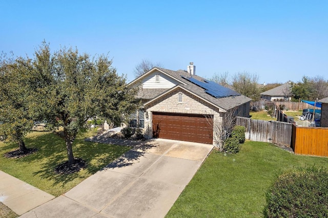 view of front of house featuring stone siding, roof mounted solar panels, fence, an attached garage, and a front yard