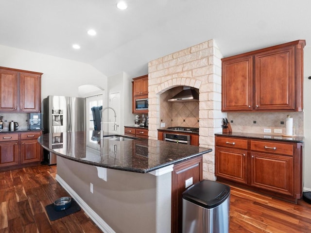 kitchen featuring dark wood-type flooring, a sink, appliances with stainless steel finishes, wall chimney range hood, and vaulted ceiling