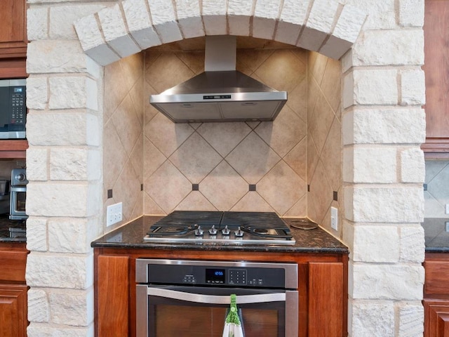 kitchen featuring tasteful backsplash, dark stone countertops, ventilation hood, and stainless steel appliances