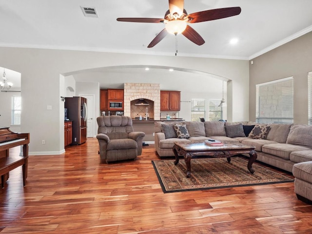 living area with crown molding, ceiling fan with notable chandelier, visible vents, and light wood finished floors