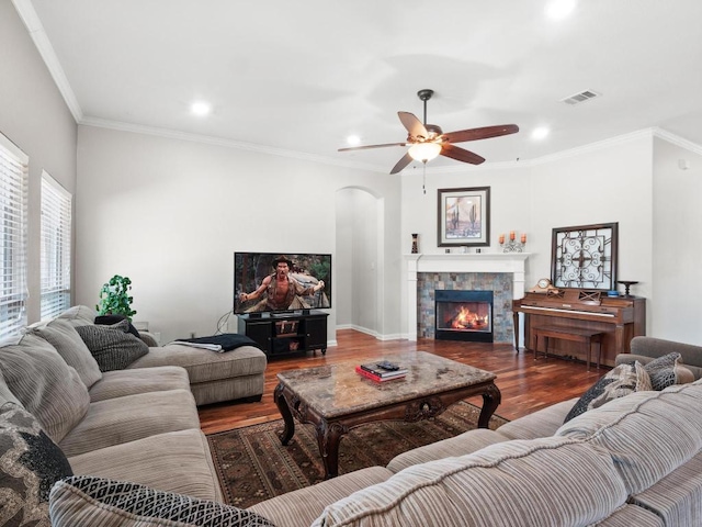 living area featuring a tiled fireplace, visible vents, ornamental molding, and wood finished floors