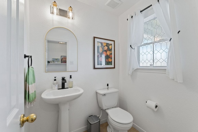 half bath featuring visible vents, toilet, and baseboards