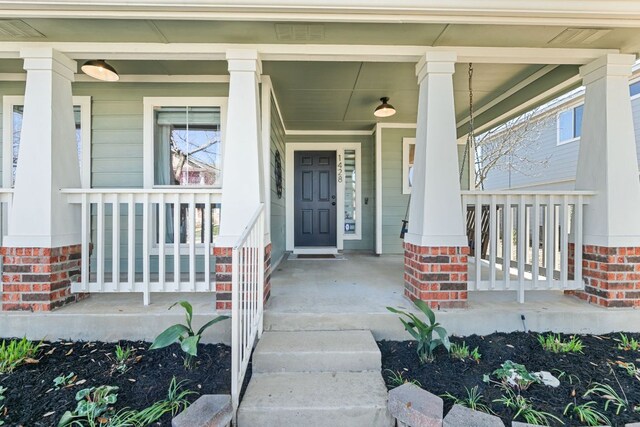 view of exterior entry with visible vents, brick siding, and a porch