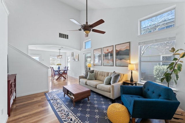 living area with wood finished floors, visible vents, baseboards, arched walkways, and a towering ceiling