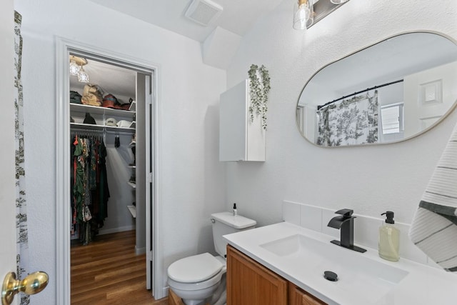 bathroom with vanity, wood finished floors, visible vents, a walk in closet, and toilet