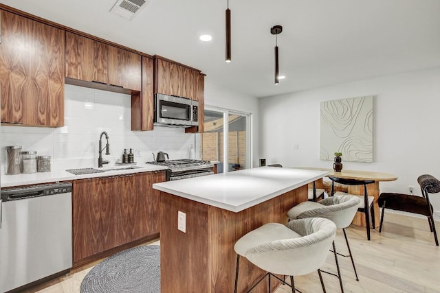 kitchen featuring visible vents, a sink, a kitchen breakfast bar, stainless steel appliances, and decorative backsplash