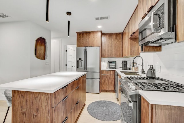 kitchen featuring brown cabinetry, visible vents, a sink, stainless steel appliances, and a center island