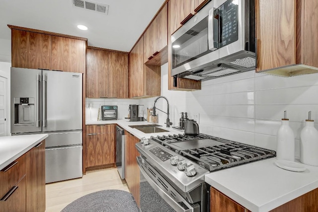 kitchen with visible vents, a sink, stainless steel appliances, light countertops, and brown cabinets