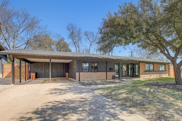 ranch-style house with fence, board and batten siding, concrete driveway, an attached carport, and brick siding