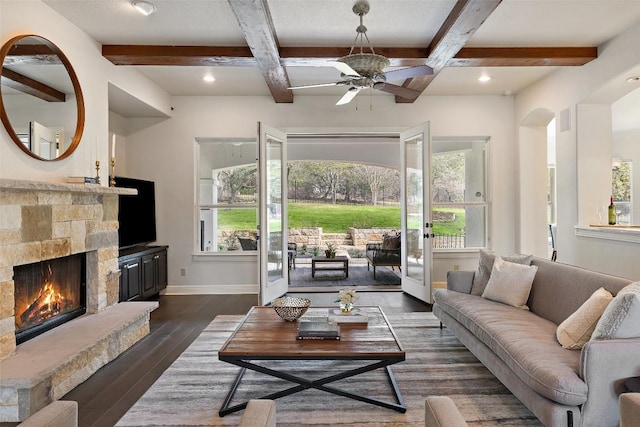 living room featuring baseboards, beamed ceiling, a stone fireplace, dark wood-style floors, and coffered ceiling