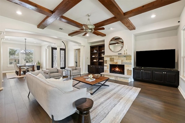 living room with baseboards, ornate columns, ceiling fan with notable chandelier, a fireplace, and dark wood-type flooring